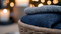 Folded knit sweaters stacked in wicker basket with warm bokeh lights and candles in background, cozy home decor.