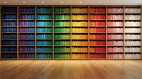 Colorful rainbow bookshelf wall with organized books arranged by color spectrum from blue to red in modern library or study room interior.