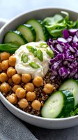 Fresh buddha bowl with chickpeas, quinoa, cucumber slices, red cabbage, and creamy yogurt sauce garnished with green onions. Healthy vegetarian lunch.