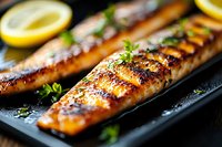 Grilled salmon fillet with caramelized glaze and fresh herbs on black slate plate, garnished with lemon slices, macro food photography with selective focus.