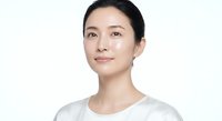 Young Asian woman with natural makeup and pulled back hair wearing white shirt on clean background for skincare and beauty concepts.