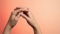Two hands gently touching fingertips in prayer or meditation gesture against coral pink gradient background for wellness and mindfulness concepts.