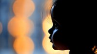 Dramatic silhouette profile of young girl against blurred warm bokeh lights background creating dreamy atmospheric mood for emotional storytelling and childhood concepts.