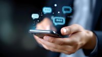 Person holding smartphone with glowing chat bubbles floating above screen, depicting digital communication and messaging technology in dark background.