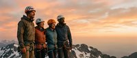 Group of four mountaineers in winter gear standing on snowy alpine peak at sunset, displaying teamwork and adventure spirit for outdoor expedition and climbing content.