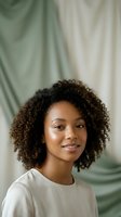 Young African American woman with curly hair smiling confidently in natural light with soft green fabric background for lifestyle and wellness content.