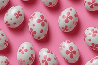 White Easter eggs decorated with pink floral patterns and polka dots arranged on pink background creating festive holiday composition with soft shadows.