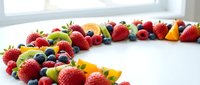Fresh mixed berries and fruits arranged on white surface with natural lighting for healthy eating and nutrition concepts.