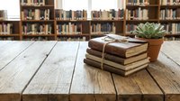 Stack of vintage books tied with twine and potted succulent plant on wooden table in library with bookshelves background for education and reading concepts.