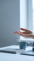 Open palm hand gesture of a woman at a bright workspace with coffee mug and notebook, expressing welcome, agreement, or presentation for business and corporate concepts.