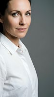 Professional middle-aged Caucasian businesswoman in white shirt looking confident with natural makeup and pulled back hair against gray background.