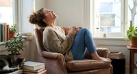 Young woman relaxing in cozy armchair by window with coffee cup, enjoying peaceful moment at home. Casual lifestyle and comfort concept.