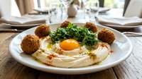 Middle Eastern hummus plate with crispy falafel balls, fresh herbs and olive oil drizzle served in elegant restaurant setting for Mediterranean cuisine menu.