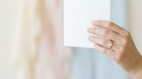 Person holding blank white card or paper against soft blurred background, suitable for mockups, advertising, and promotional designs.