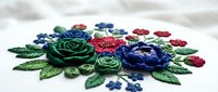 Colorful embroidered flowers with green leaves on white fabric, featuring red, blue, and green thread work. Isolated design element suitable for textile, craft, and decorative projects.