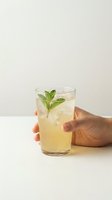 Hand holding a glass of iced lemonade with fresh mint garnish on a white background, refreshing summer drink concept.