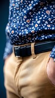 Close-up of floral navy blue shirt tucked into beige pants with black leather belt, showcasing classic menswear style detail and pattern contrast.