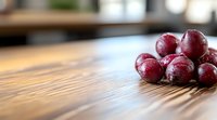 Fresh red grapes with water drops on wooden table surface, selective focus with blurred background creating minimalist food composition.