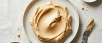 Creamy peanut butter swirl in white ceramic bowl with spreading knife on neutral surface, ready for cooking and baking projects.