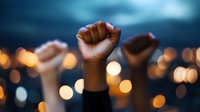 Raised fists silhouetted against evening sky with defocused city lights, symbolizing unity, protest, solidarity and social movement activism in urban setting.