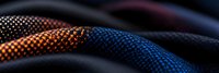 Macro shot of colorful climbing rope texture showing detailed nylon braided pattern against dark background, highlighting orange and blue woven fibers.