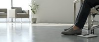 Professional businessman legs in dress shoes under office desk in modern workplace with minimalist furniture and polished concrete floor.