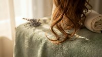 Relaxing spa setting with a woman's wavy auburn hair, soft green towel, lavender sprigs, and warm natural light for wellness themes.