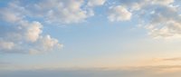 Soft pastel sky with fluffy white clouds at sunset or sunrise creating peaceful atmospheric background for meditation wellness and tranquil moments.