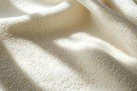 Soft waves of cream colored fabric with gentle shadows creating abstract texture and patterns. Natural sunlight adds depth to luxurious textile surface.