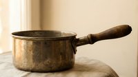 Vintage copper saucepan with wooden handle on marble surface in warm natural light for rustic kitchen cooking and culinary design projects.