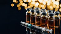 Medical vials with amber liquid and syringe against warm bokeh lights background for pharmaceutical research and healthcare applications.