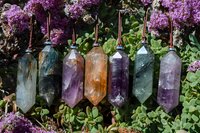 Crystal pendants with amethyst, citrine, and fluorite hanging in row against blooming lilac flowers background, spiritual healing stones and minerals for meditation.