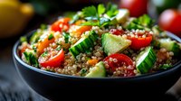 Fresh quinoa salad with cherry tomatoes, cucumber, avocado and herbs in black bowl. Healthy vegan meal with colorful vegetables and ancient grains.