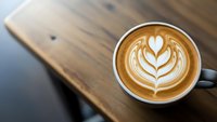 Coffee cup with heart latte art on wooden table. Cappuccino with milk foam design. Morning beverage for cafe menu, coffee shop branding and hospitality.