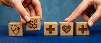 Hands arranging wooden blocks with healthcare symbols including stethoscope, gears, medical cross and heartbeat on blue background for medical services and wellness concepts.