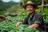 Asian male farmer smiling while tending to organic strawberry plants in greenhouse garden. Wearing straw hat and work clothes, represents sustainable agriculture.