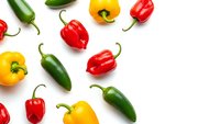 Colorful fresh peppers scattered on white background. Red bell peppers, yellow capsicum and green chili peppers arranged in pattern for cooking and healthy eating.