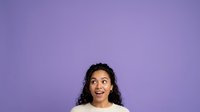Young woman with long curly dark hair and medium skin tone smiling against purple background, suitable for portraits, diversity, lifestyle, and commercial advertising projects.