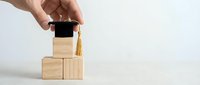 Hand placing graduation cap on wooden blocks symbolizing education achievement and academic success journey for career development.
