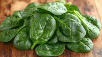 Fresh organic spinach leaves pile on rustic wooden cutting board for healthy cooking and nutrition. Natural green leafy vegetables for salads and meals.