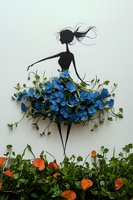 Elegant female silhouette with flowing hair wearing dress made of blue flowers and green leaves on white background for creative design projects.