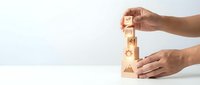 Hands carefully stacking wooden blocks with business icons representing growth strategy and development planning for corporate success and teamwork.