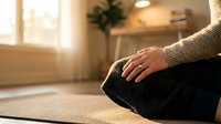 Woman practicing meditation in cozy home setting with warm natural lighting and comfortable cushion for mindfulness and relaxation wellness routine.