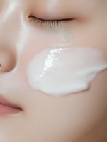 Close-up of smooth facial skin with white cream texture, showing moisturizer application on cheek. Clean minimalist beauty and skincare concept.