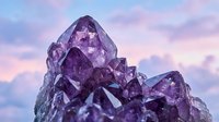Purple amethyst crystal cluster formation against dreamy pastel sky background for healing meditation and spiritual wellness concepts.