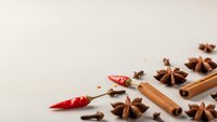 Aromatic spices scattered on neutral background with cinnamon sticks, star anise, red chili peppers and cloves for culinary cooking and food preparation.