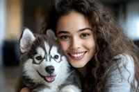 Happy young woman with curly hair embracing adorable husky puppy with blue eyes in cozy home interior for pet adoption and companionship concepts.