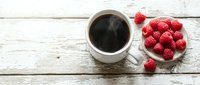 Cup of black coffee with fresh raspberries on white wooden table, overhead view for food and beverage design, cafe menu, recipe blogs.