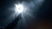 Glowing shield with checkmark radiating light rays above an outstretched hand on dark background, symbolizing cybersecurity and digital protection.