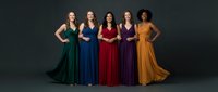 Five diverse women in elegant colorful evening gowns standing together against dark background for formal events, fashion, and celebration concepts.
